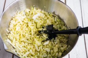 green cabbage in a bowl with a potato masher