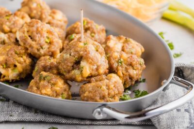 juicy, cheesy sausage balls stacked on each other in a skillet with a toothpick in the top one