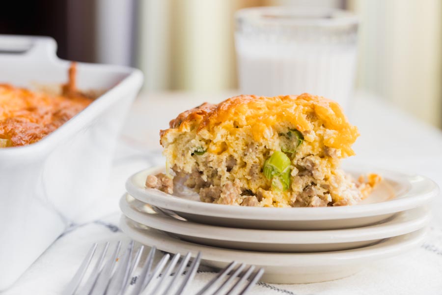 cheesy casserole on a plate with a green onion sliding down and a glass of milk behind the plate