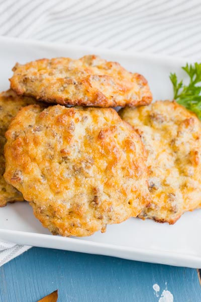 A pile of cheddar and sausage biscuits on a plate with a sprig of parsley.