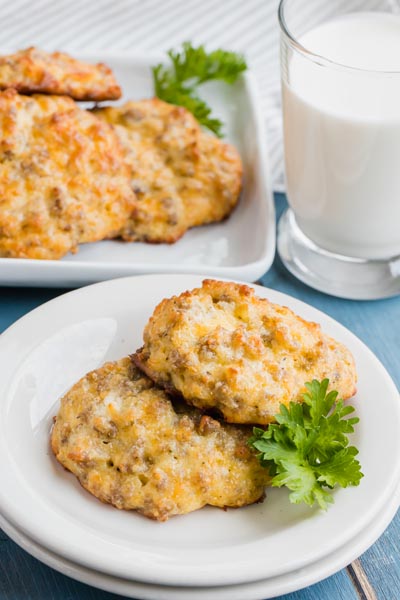 Two cheddar biscuits on a plate next to parsley and a glass of milk.