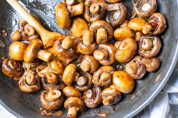 sauteed mushrooms in a cast iron skillet with a wooden spoon