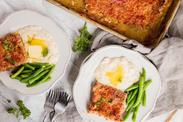 two plates of dinner with keto meatloaf and a pan of meatloaf next to it