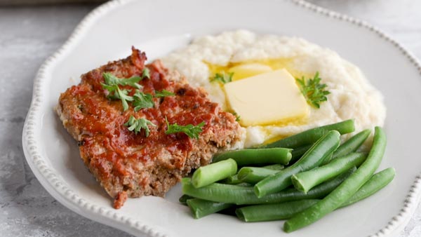 a slice of meatloaf with a side of mashed cauliflower and green beans