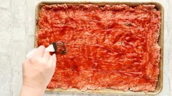 brushing red sauce on sheet pan meatloaf