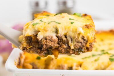 A slice of shepherd's pie on a spatula with grease dripping from it in a good way.