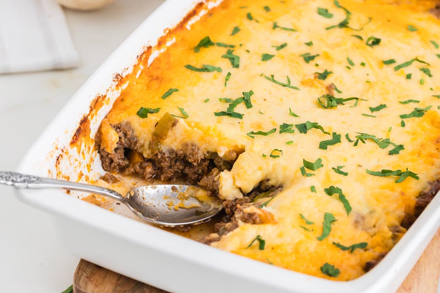 A silver spoons rests in a casserole dish filled with shepherds pie.