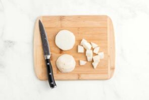 Diced turnips on a wooden cutting board next to a knife.
