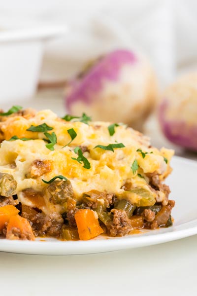 Close up of mashed turnips over meat filling on a plate.