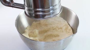 sifter with flours over a metal bowl