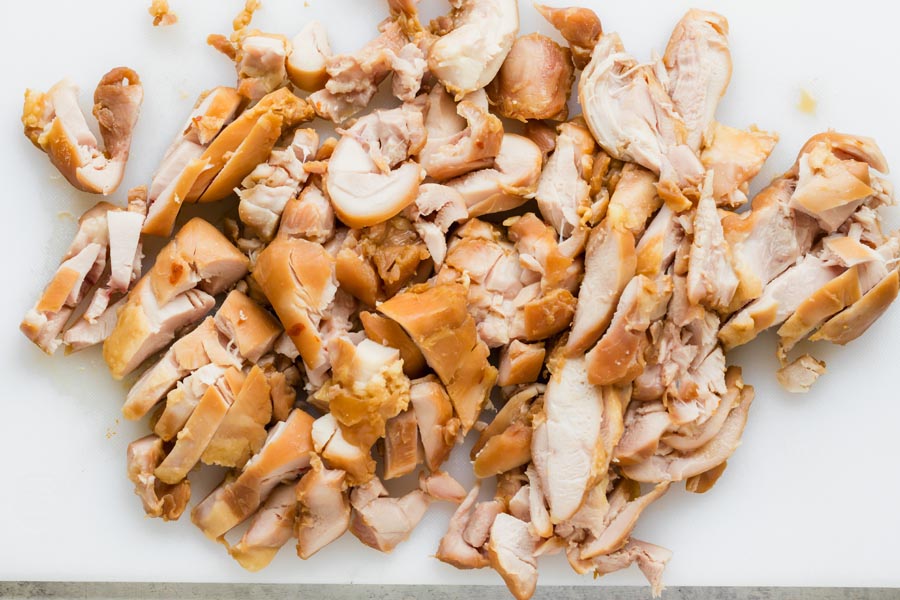 Chopped cooked chicken pieces spread out on a cutting board, ready to be served or added to a dish.