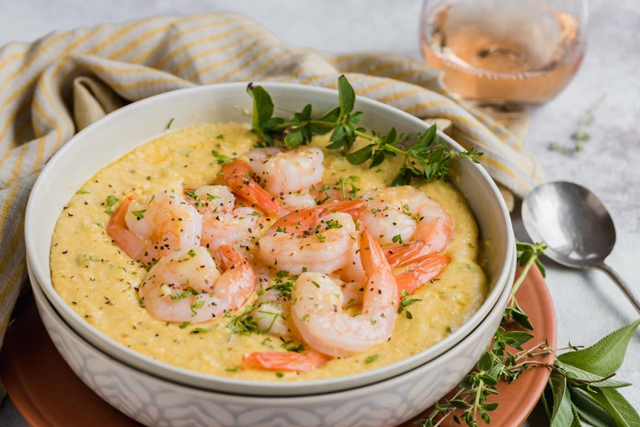 a bowl of shrimp and grits next to a glass of wine