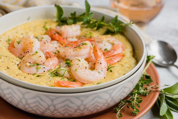 a bowl of grits with cooked shrimp on top and chopped herbs