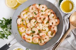 shrimp cooking in a skillet next to melted butter