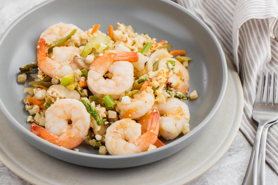 a bowl of shrimp fried cauliflower rice with a fork next to it