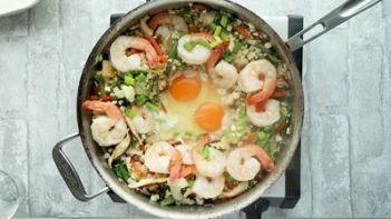 two eggs cracked in the center of a skillet with vegetables and shrimp off to the side