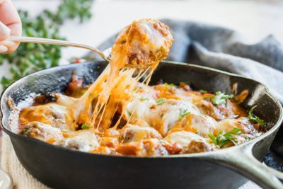 pulling a single meatball out of a skillet with cheese pulling down