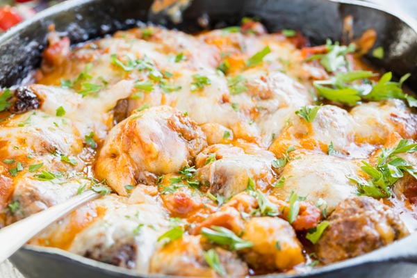 a skillet with meatballs and melted cheese topped with parsley