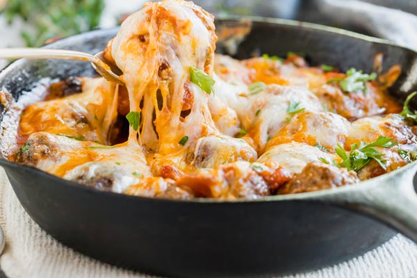 pulling a cheesy meatball out of a cast iron skillet