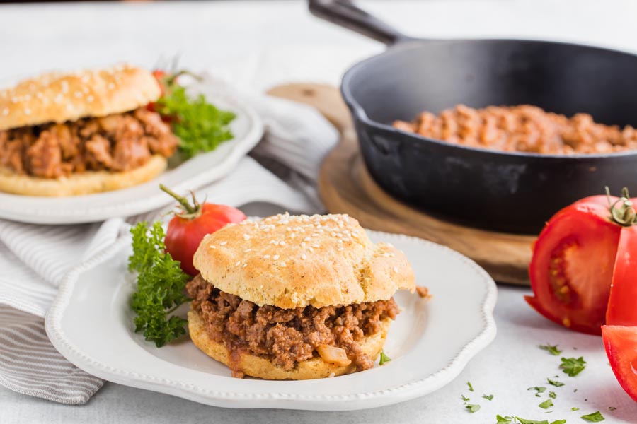 two plates with sloppy joe sandwiches on them and a skillet behind