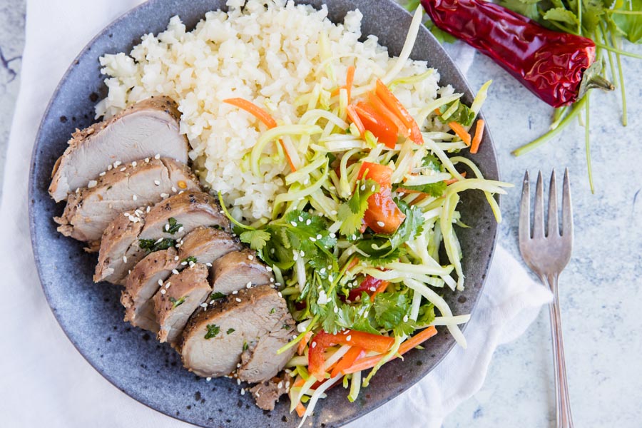 slices of keto asian pork tenderloin with a cauliflower rice and salad on a plate