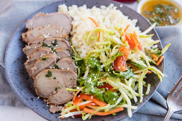 plated of sliced marinated keto pork tenderloin next to cauli rice and broccoli slaw