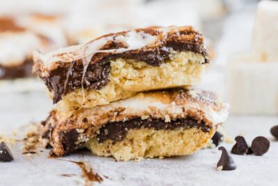 smores bars with layers of graham cracker, chocolate and marshmallow next to a few chocolate chips