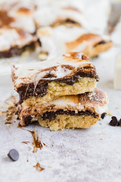 smores bars stack on each other with chocolate smeared on the counter and melted marshmallow coming down