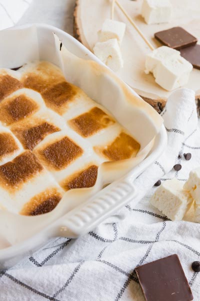 toasted marshmallows in a baking dish with chocolate and marshmallows surrounding
