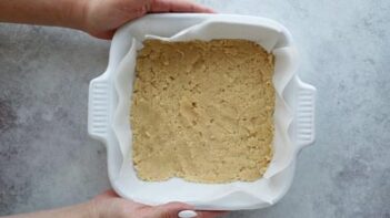 holding a square baking dish with a crust pressed into it