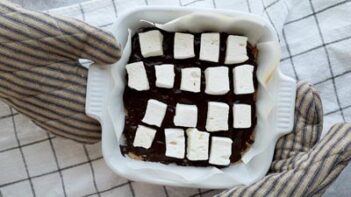 marshmallows placed on top of melted chocolate in a square baking dish