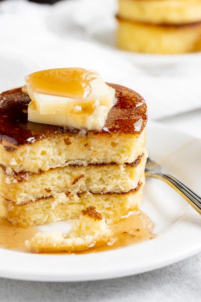 a stack of pancakes cut through with syrup dripping down and topped with butter