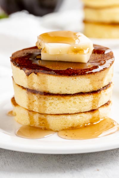 breakfast stack of pancakes that are very thick and fluffy and topped with butter and syrup