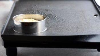 pancake batter cooking in a biscuit cutter mold on a griddle
