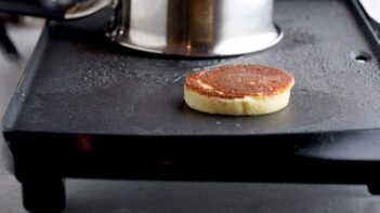 a thick pancake flipped on a griddle with a pot in the background