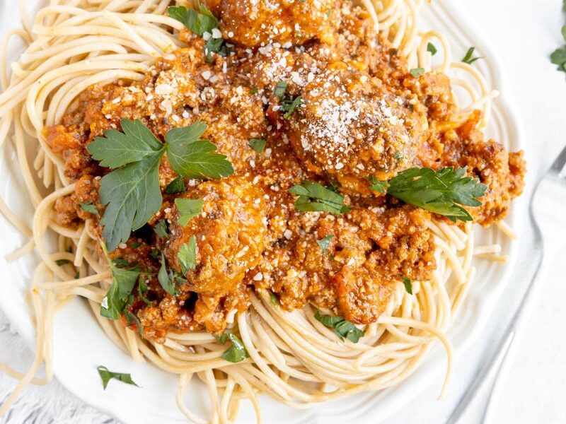 plate of spaghetti topped with grated parmesan cheese and parsley leaves