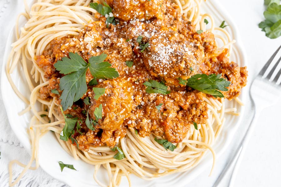 plate of spaghetti topped with grated parmesan cheese and parsley leaves