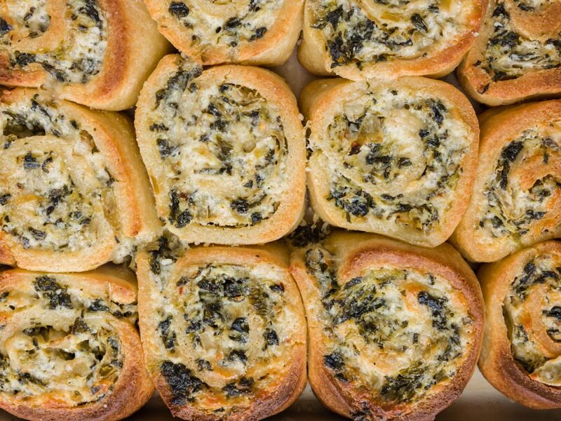 Pinwheel shaped savory spinach buns bunched together on a baking tray.