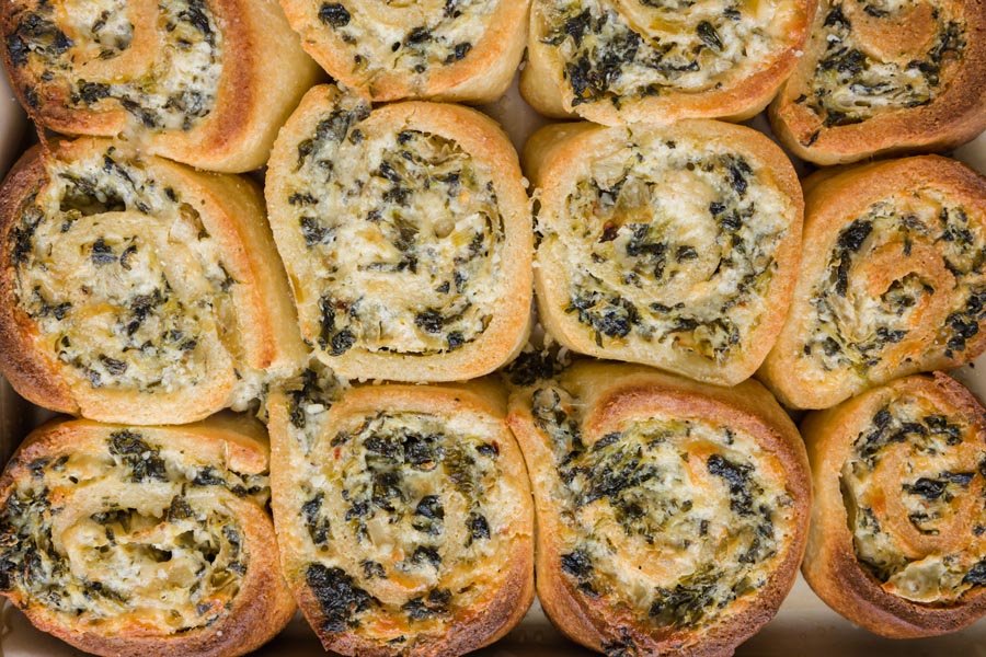Pinwheel shaped savory spinach buns bunched together on a baking tray.