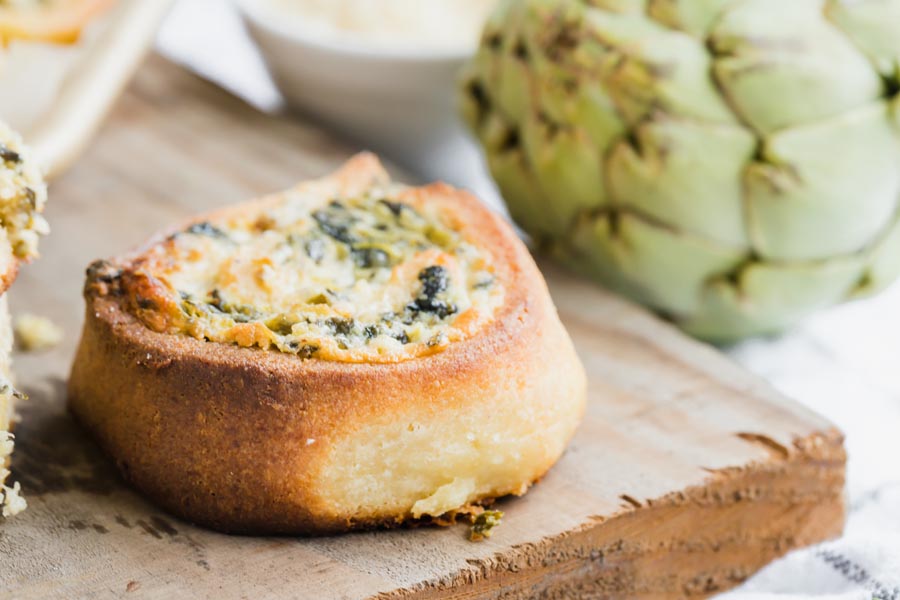 Close up of a golden spinach artichoke pinwheel bun with golden brown pastry crust.