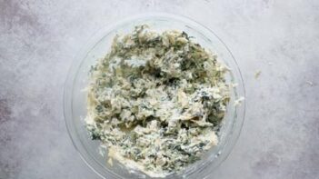 A clear bowl with creamy spinach artichoke mixture inside.