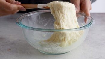 A hold pulling melted mozzarella cheese out of a bowl using a spatula.