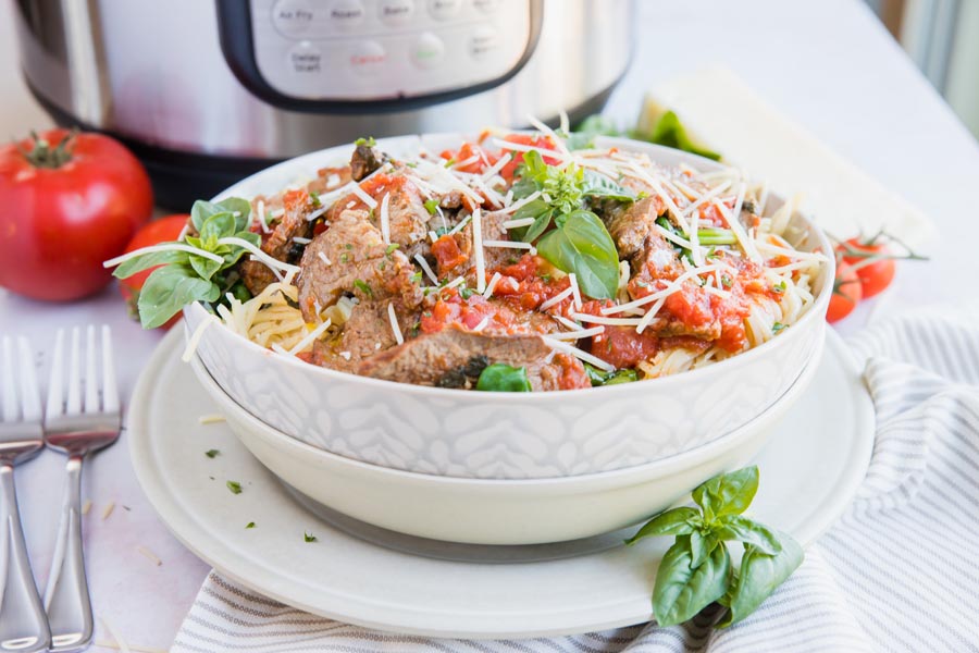 a big bowl of pasta sitting in front of an instant pot with basil and tomatoes around