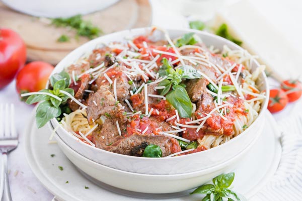 a bowl stacked on a another bowl containing a red sauced pasta topped with basil and parmesan cheese