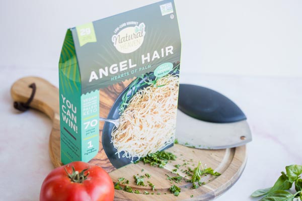 keto hearts of palm noodles on a cutting board with basil and tomatoes