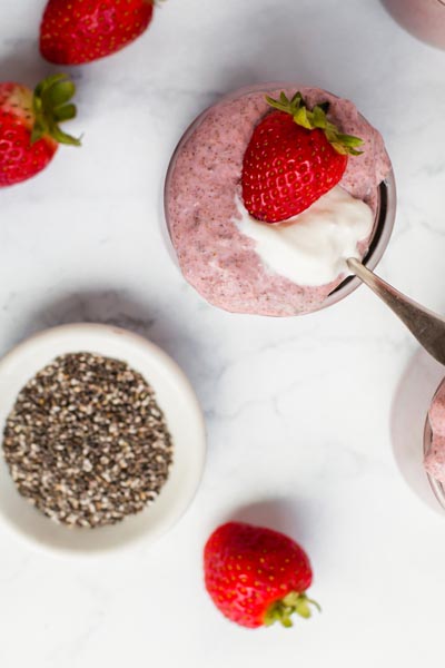 looking down onto a small jar of chia pudding with a strawberry on top next to a dish with chia seeds
