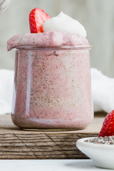 close up of a jar of strawberry chia pudding topped with whipped cream and a slice of strawberry