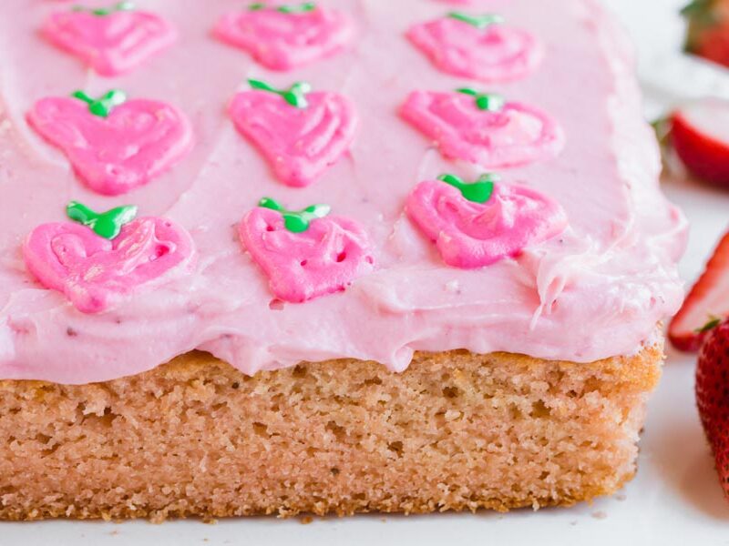 a full strawberry cake with pink frosting decorated with strawberries made out of frosting