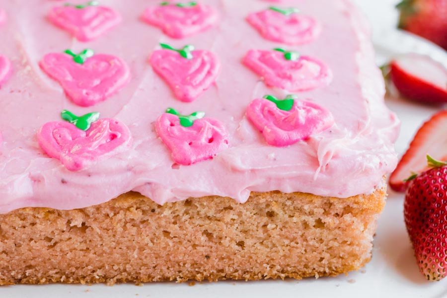 a full strawberry cake with pink frosting decorated with strawberries made out of frosting