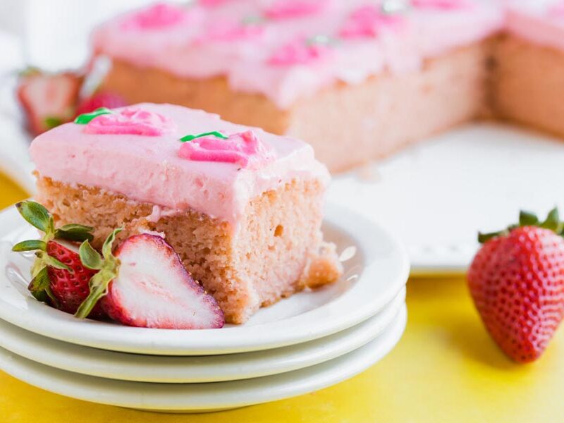 slice of strawberry cake on a stack of white plates with strawberries around